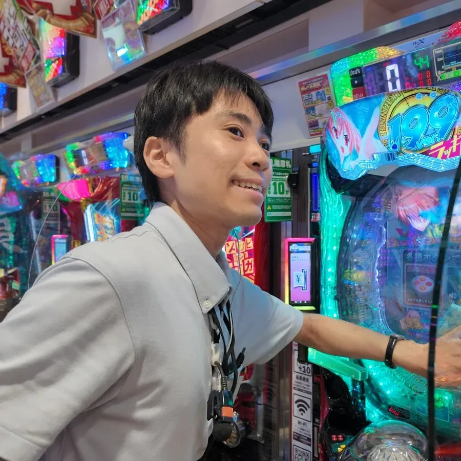 アミューズメント事業部の社員が遊技台のそばで笑顔を見せている様子